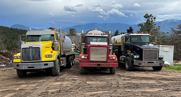 Three semi trucks one yellow, one red, one black.