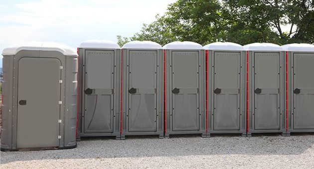 A row of beige portable toilets with orange trim. At one end of the row is a handicap accessible portable toilet.
