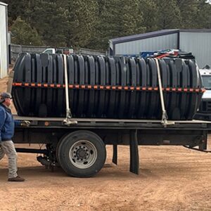 A truck trailer holds a septic tank. A man walks beside the trailer.