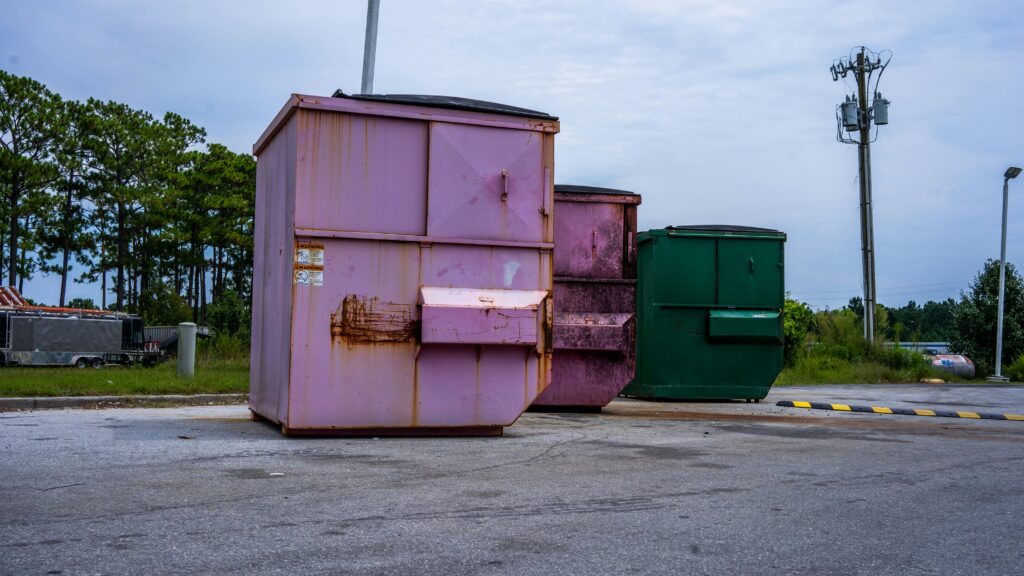 Three portable dumpsters, two pink and one green.